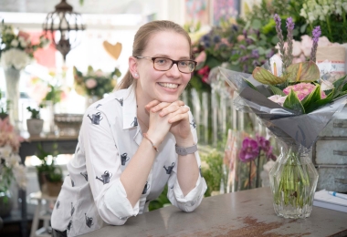 Florist sitting in shop with a perfectly finished flower arrangement in a vase