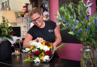 Florist in shop making a sunflower featured wrap of flowers layed on worktop