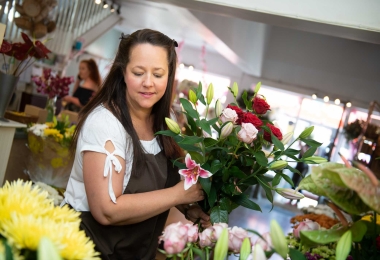 Florist wearing brown apron choosing flowers for a hand-tied