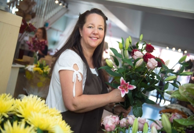 Florist in shop making a bouquet featuring pink and red roses surrounded by flowers