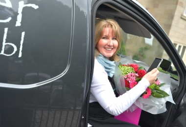 Florist in grey van, getting out holding a vibrant pink bouquet and phone