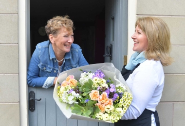 Smiling woman receiving a colourful bouquet of flowers at her front door from a florist.