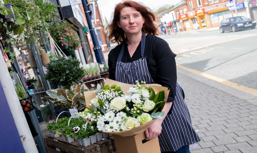 Florist in a striped apron outside a flowershop holding a cream themed boxed hand-tied.