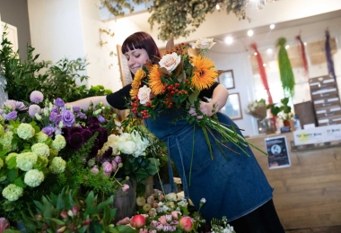Florist in shop wearing denim apron choosing flowers for an autumn themed bouquet.