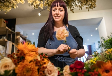 Florist holding a single Autumn stem with seasonal flowers layed out on the table