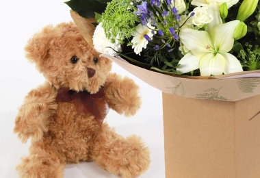 Close-up of a luxury hand-tied with white and blue flowers on a white background with a brown teddy bear.