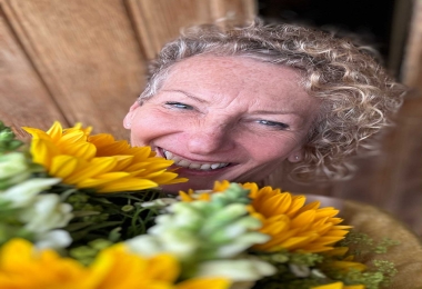 Cropped selfie of a happy woman hugging a delivery of sunflowers at a front door.