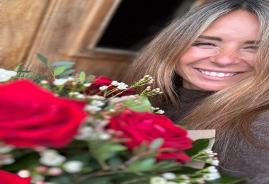 Cropped selfie of a happy woman holding red rose hand-tied at front door.