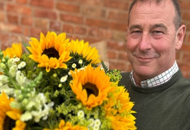 Selfie of a smiling middle-aged man hugging a vibrant box of flowers
