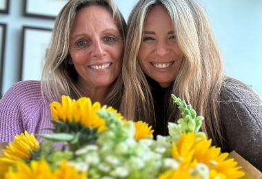 Two happy women with a bokeh sunflower arrangement in the foreground